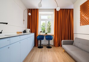 A modern kitchen with a window, two bar stools, and a grey sofa. - Zachariasza Harmony Apartment (Warszawa)