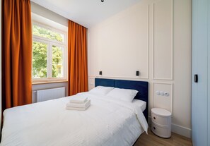 A hotel room with a bed, a radiator, a window with curtains, and a bedside table. - Zachariasza Harmony Apartment (Warszawa)
