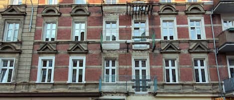 Un edificio de varios pisos con una hilera de ventanas, algunas con balcones, y una entrada a nivel de calle.