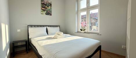 Un dormitorio con cama, mesita de noche, ventana con vistas y un reloj de pared.