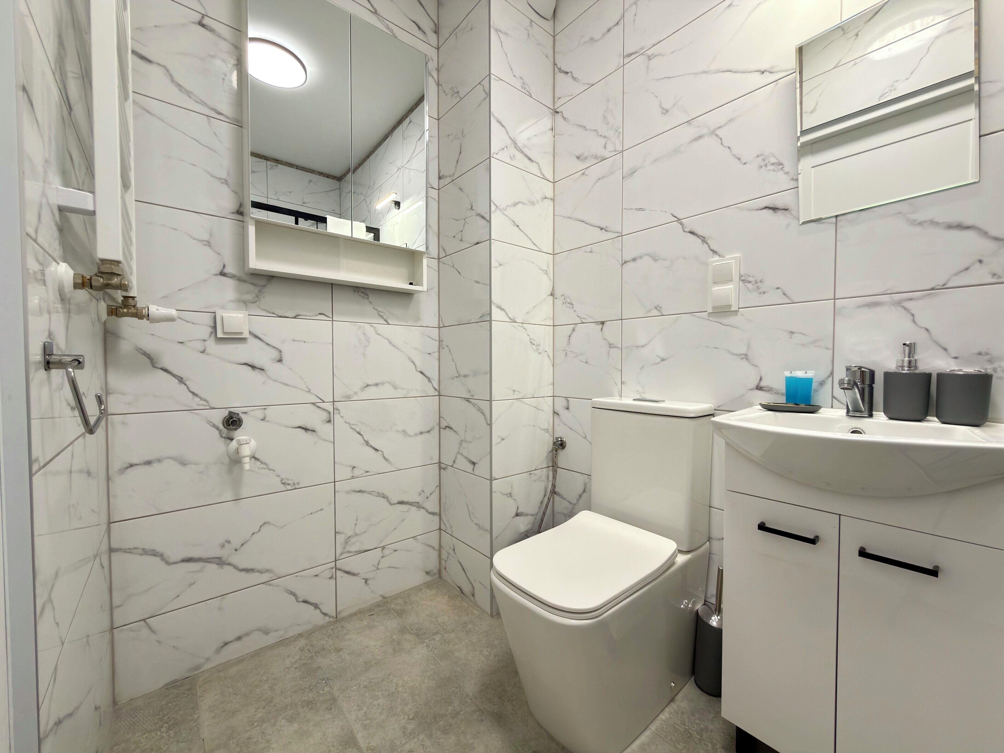 A bathroom with a toilet, sink, mirror, and marble tiles.