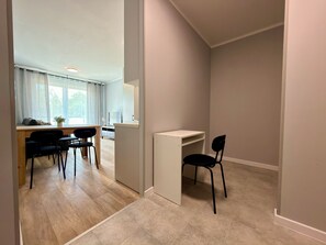Una habitación moderna y minimalista con piso de madera, un escritorio blanco, una silla negra y una zona de comedor con mesa y sillas.