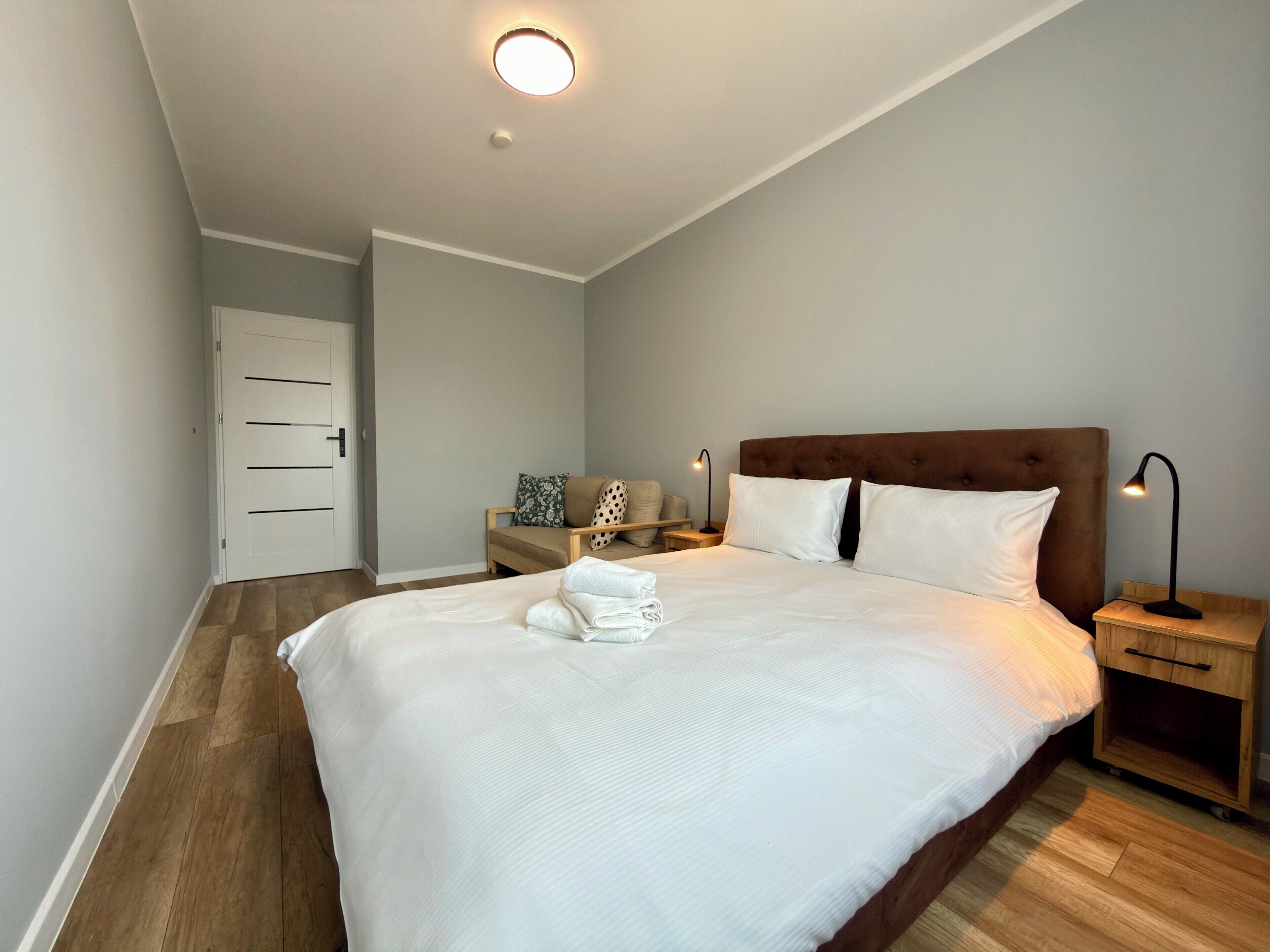 A bedroom with a large bed, bedside tables, a nightstand, a door, and a ceiling light.