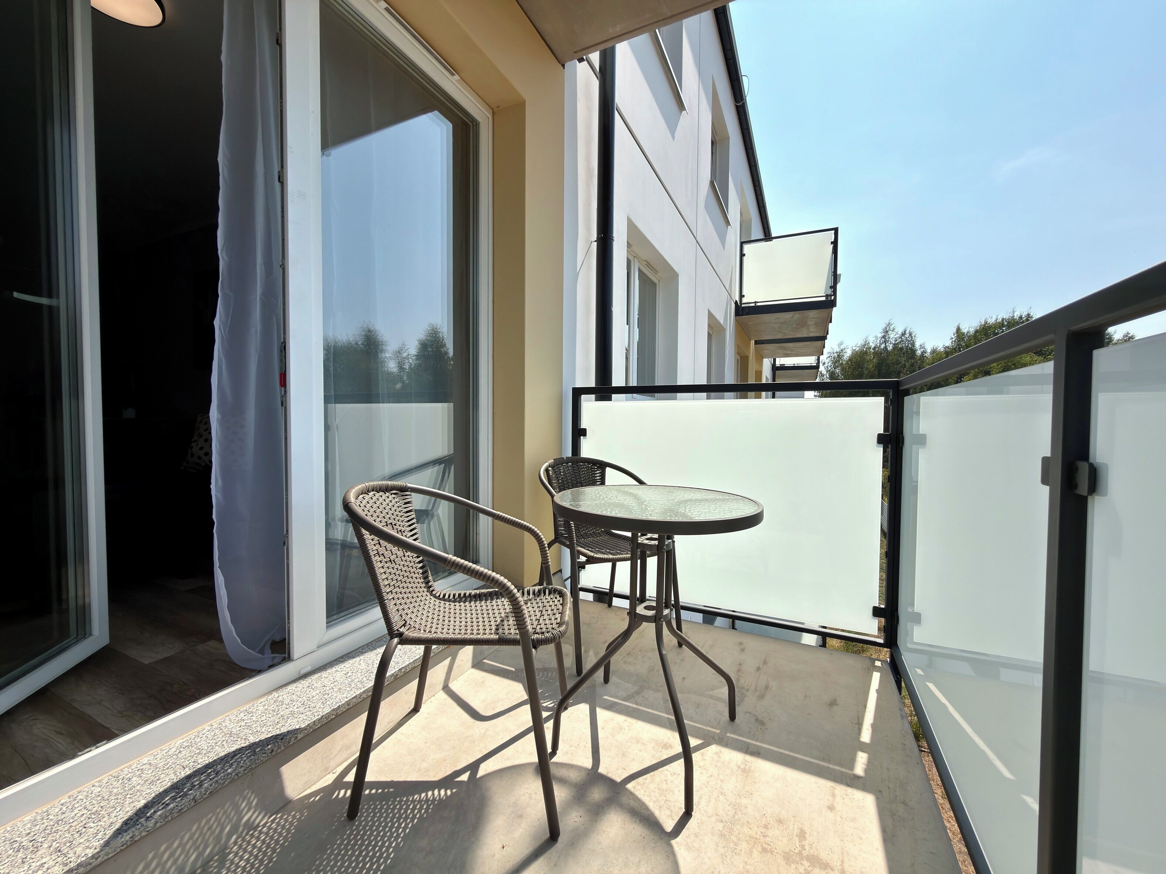 A balcony with a table and two chairs, a sliding glass door, and a view of the sky.