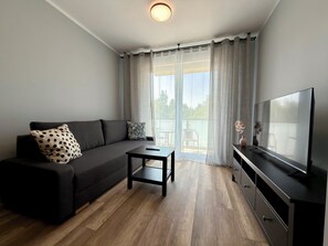 A modern living room with a sofa, a coffee table, a TV, and a balcony with a view. - Aleja Platanowa Superior Apartment (Wrocław)