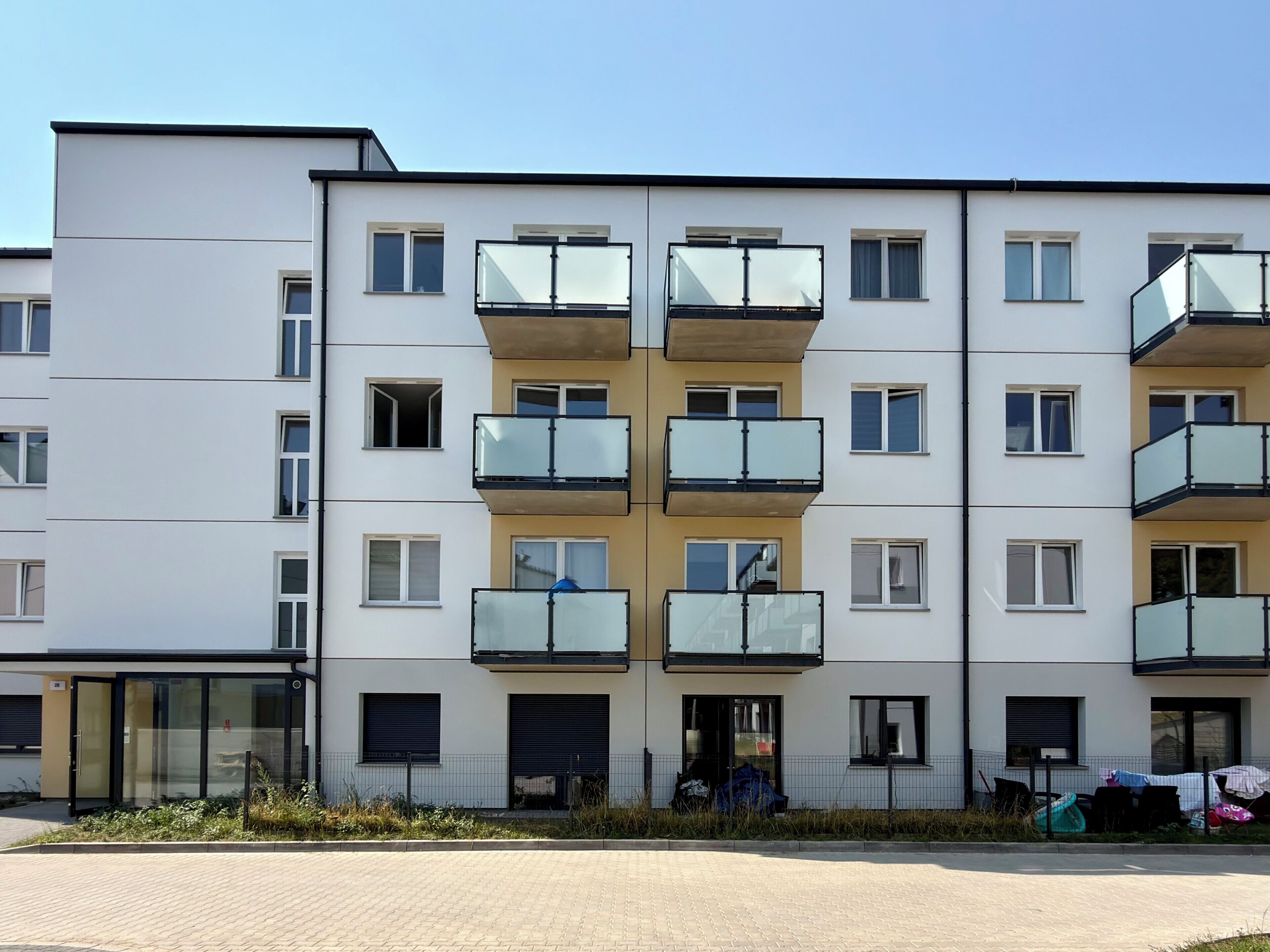 A multi-story residential building with balconies, a gated entrance, and a paved driveway.