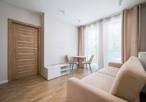 A modern living room with a wooden door, a white sofa, a small table, and a window with curtains. - Kłobucka Harmony Apartment (Warszawa)
