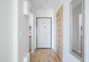 Ein Flur mit einer weißen Tür, Holzboden und einem Spiegel auf der rechten Seite.