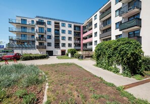 Ein mehrstöckiges Wohngebäude mit Balkonen, einem gepflasterten Innenhof und einem roten Auto vor der Fassade.