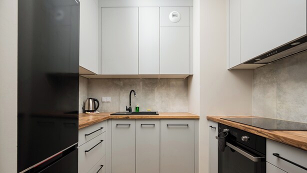 Eine kleine Küche mit einem schwarzen Kühlschrank, einem eingebauten Ofen und einer Holz Arbeitsplatte.