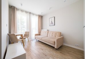 Un salon moderne avec un canapé beige, une table à manger avec deux chaises et une grande fenêtre avec des rideaux.