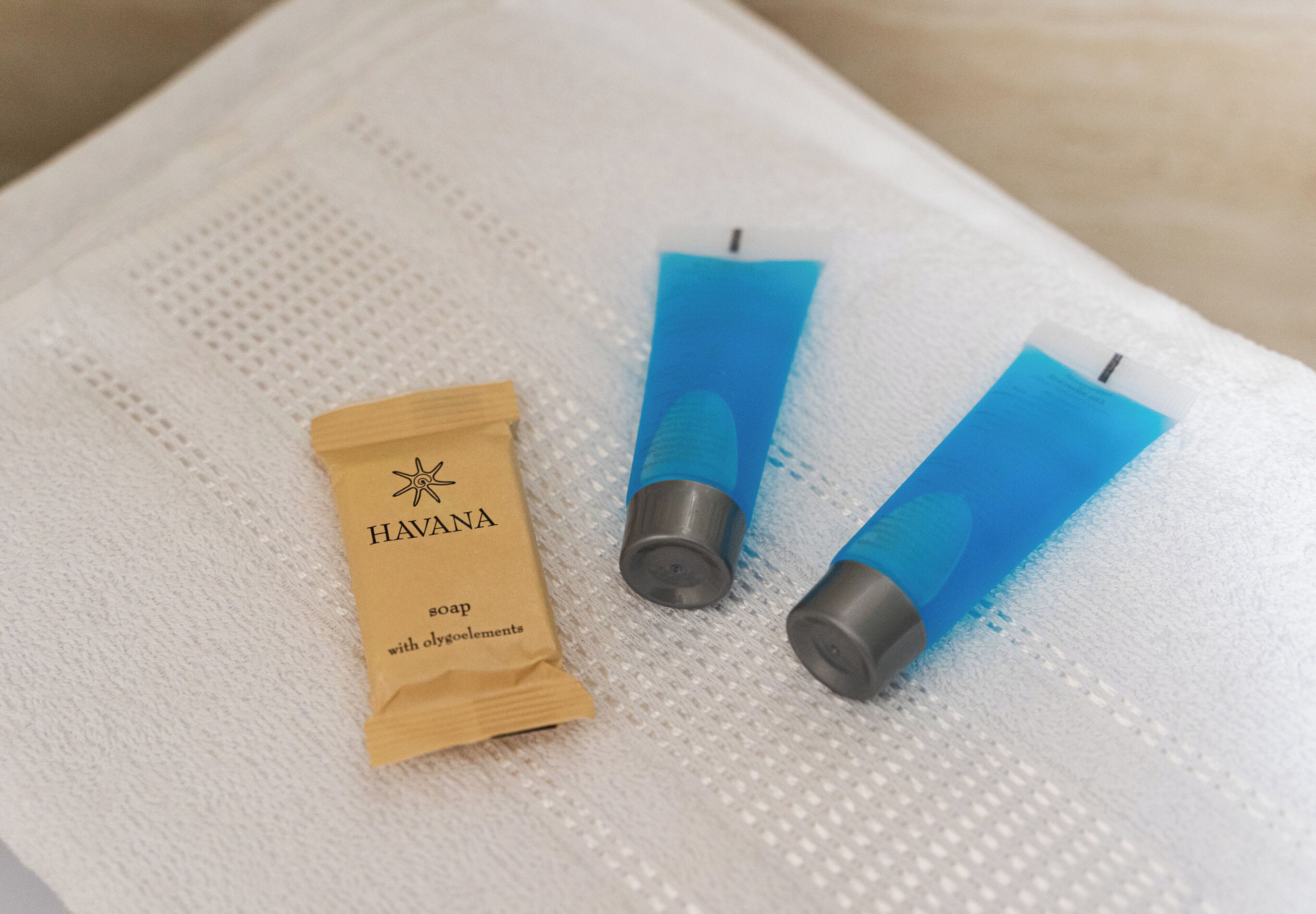 A small brown tube labeled 'HAVANA soap with oxybeliefs' and two blue tubes on a textured white surface.