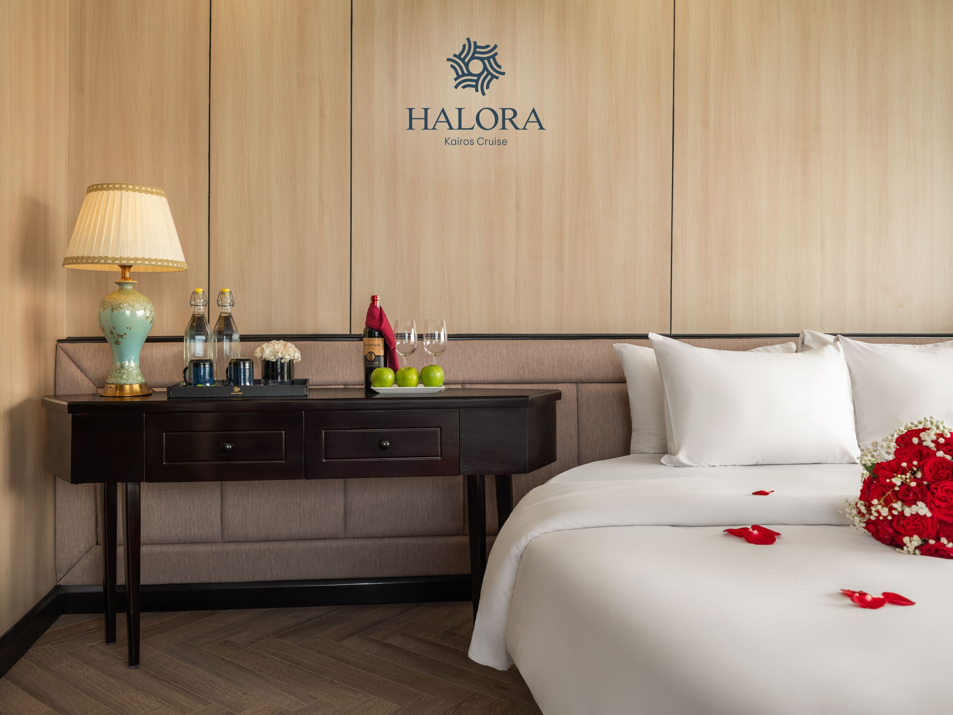 Habitación de hotel con cama, mesita de noche, lámpara y logotipo en la pared.