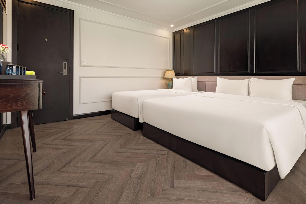 Una habitación de hotel con dos camas, un escritorio con un florero y un armario de madera oscura.