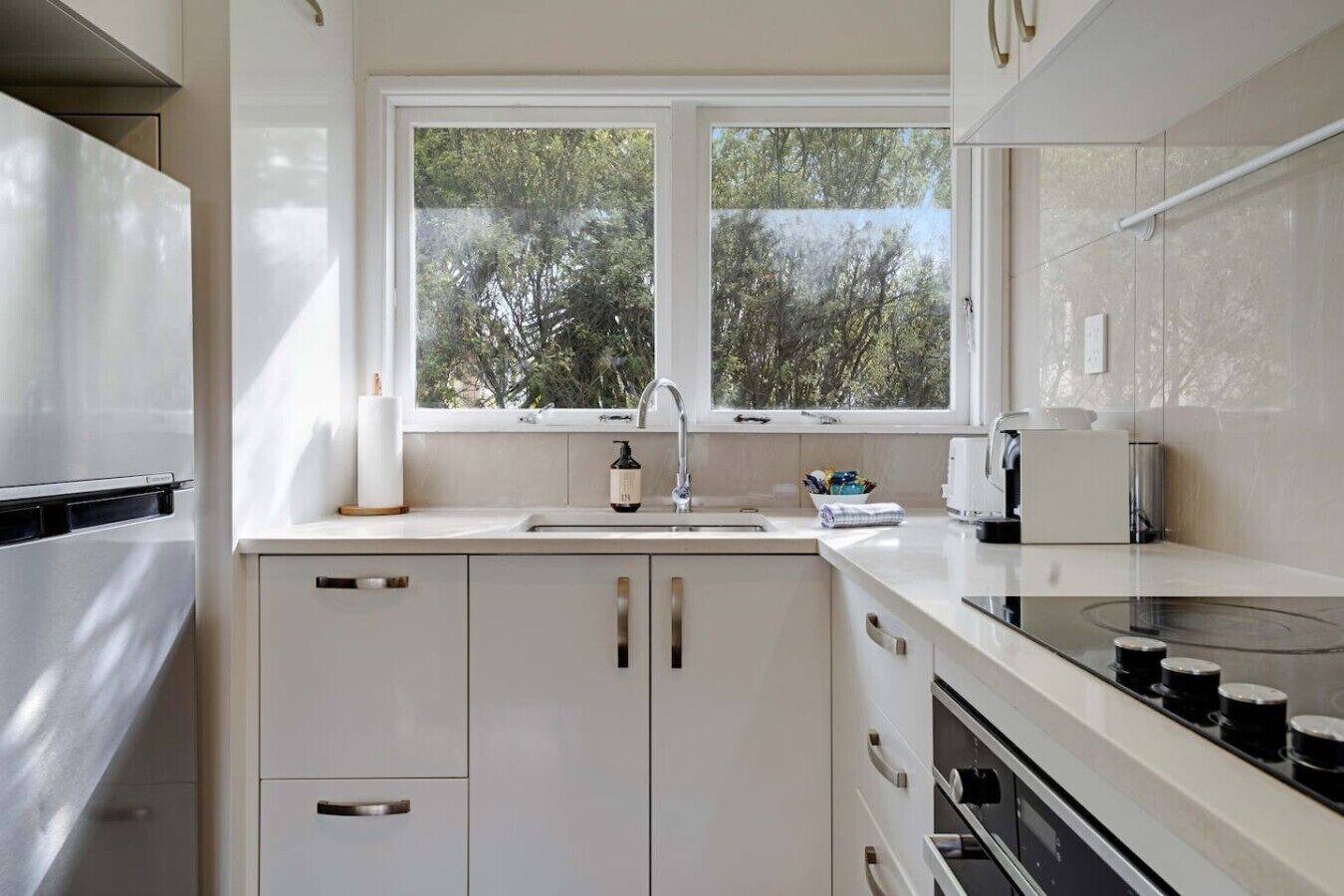 A modern kitchen with white cabinetry, a double sink, and a window overlooking greenery.