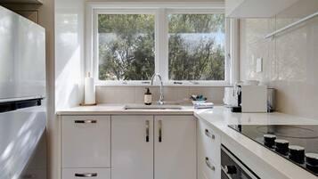 A modern kitchen with white cabinetry, a double sink, and a window overlooking greenery.