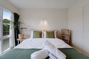 A hotel room with a bed, a bedside table with a lamp, a plant, and a window with curtains. - Sunny Greenlane Gem with Parking and Air-Con (Auckland Central Suburbs)