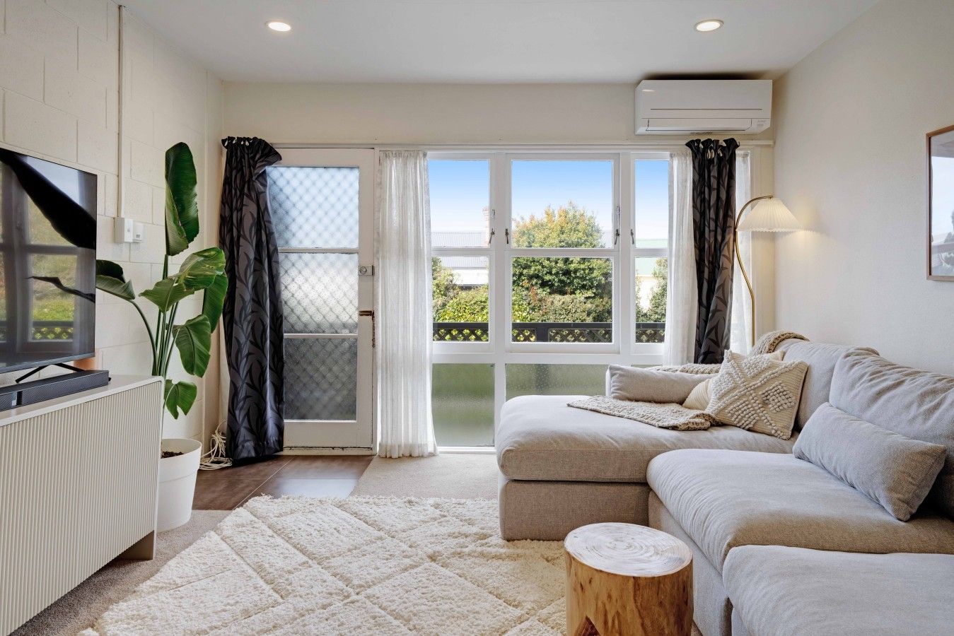 A modern living room with a sofa, a TV, a radiator, and a large window with curtains.