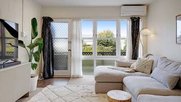 A modern living room with a sofa, a TV, a radiator, and a large window with curtains.