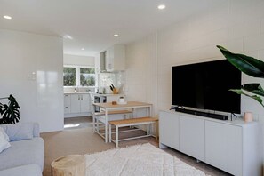 A modern living room with a flat-screen TV, a dining area with a table and benches, and a kitchen in the background. - Sunny Greenlane Gem with Parking and Air-Con (Auckland Central Suburbs)