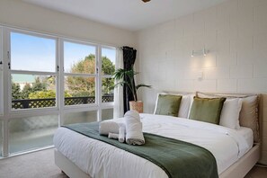A bedroom with a large bed, a view through a sliding door, and a potted plant. - Sunny Greenlane Gem with Parking and Air-Con (Auckland Central Suburbs)