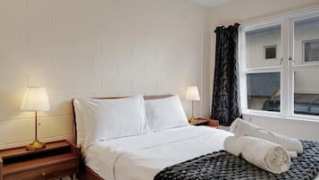 A hotel room with a bed, two bedside tables, lamps, a window with curtains, and a view of the outside.