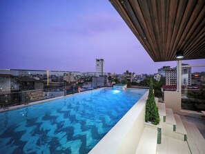 Una piscina en la azotea con vista a la ciudad, rodeada de edificios y un cielo despejado.