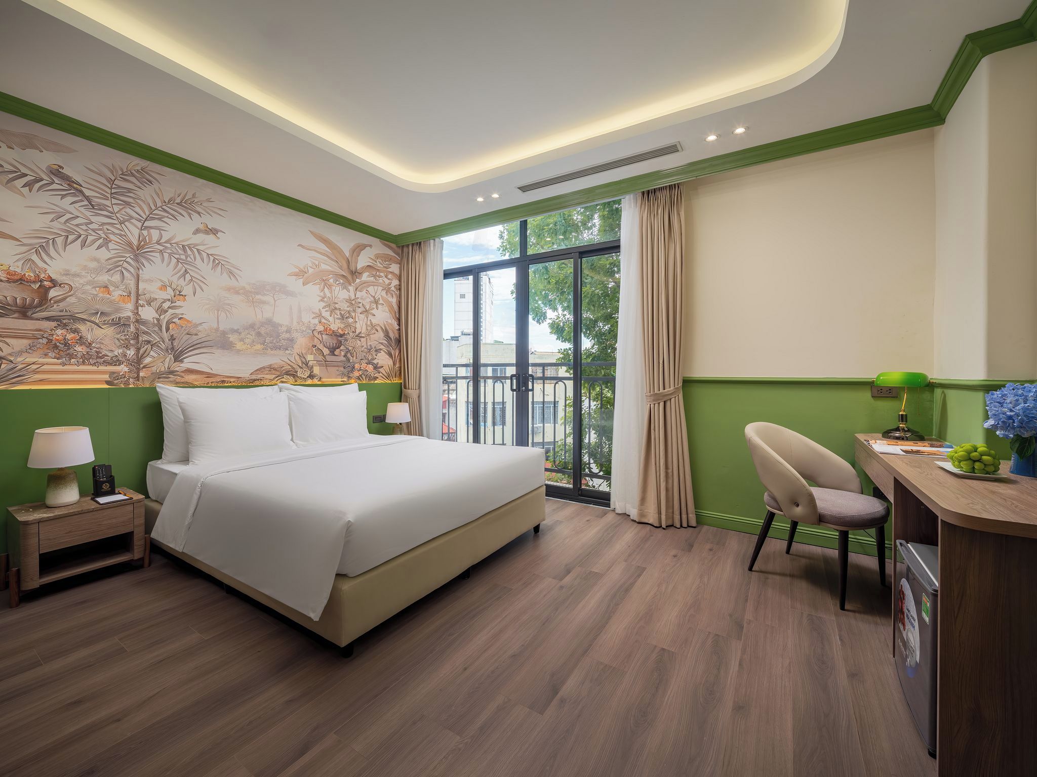 A hotel room with a large bed, a desk with a chair, a window with curtains, and a mural on the wall.