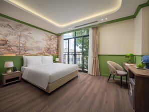 Habitación de hotel con una cama grande, un escritorio con silla, una ventana con cortinas y un mural en la pared.