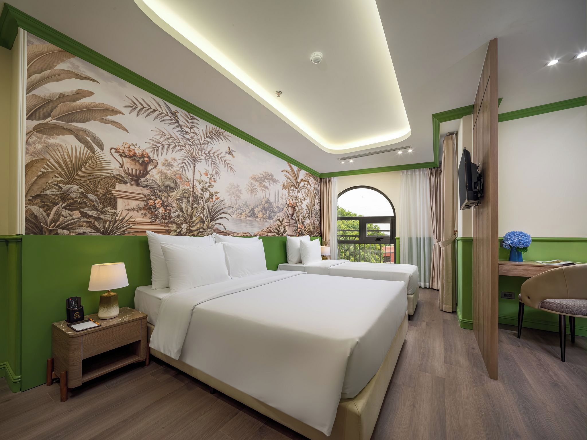 A hotel room with a large bed, a desk, a chair, a TV, and a mural on the wall.