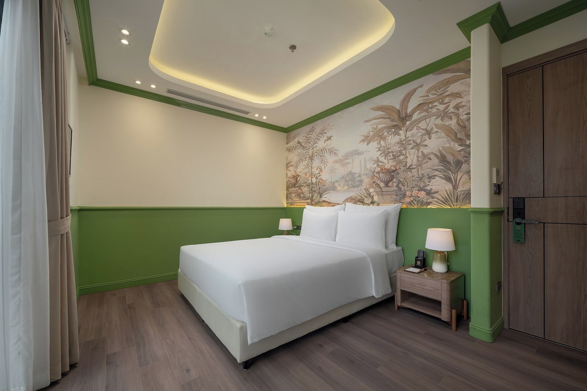 Habitación de hotel con una cama grande, mesitas de noche con lámparas, una pared de acento verde y un armario de madera.