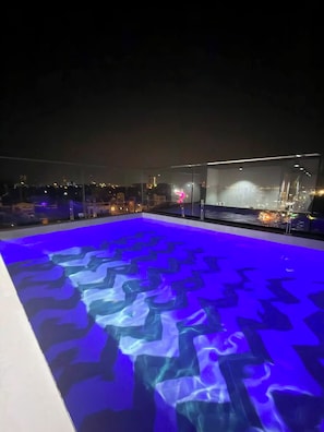 Una piscina al aire libre con un diseño geométrico en el suelo, rodeada por una barandilla de cristal.