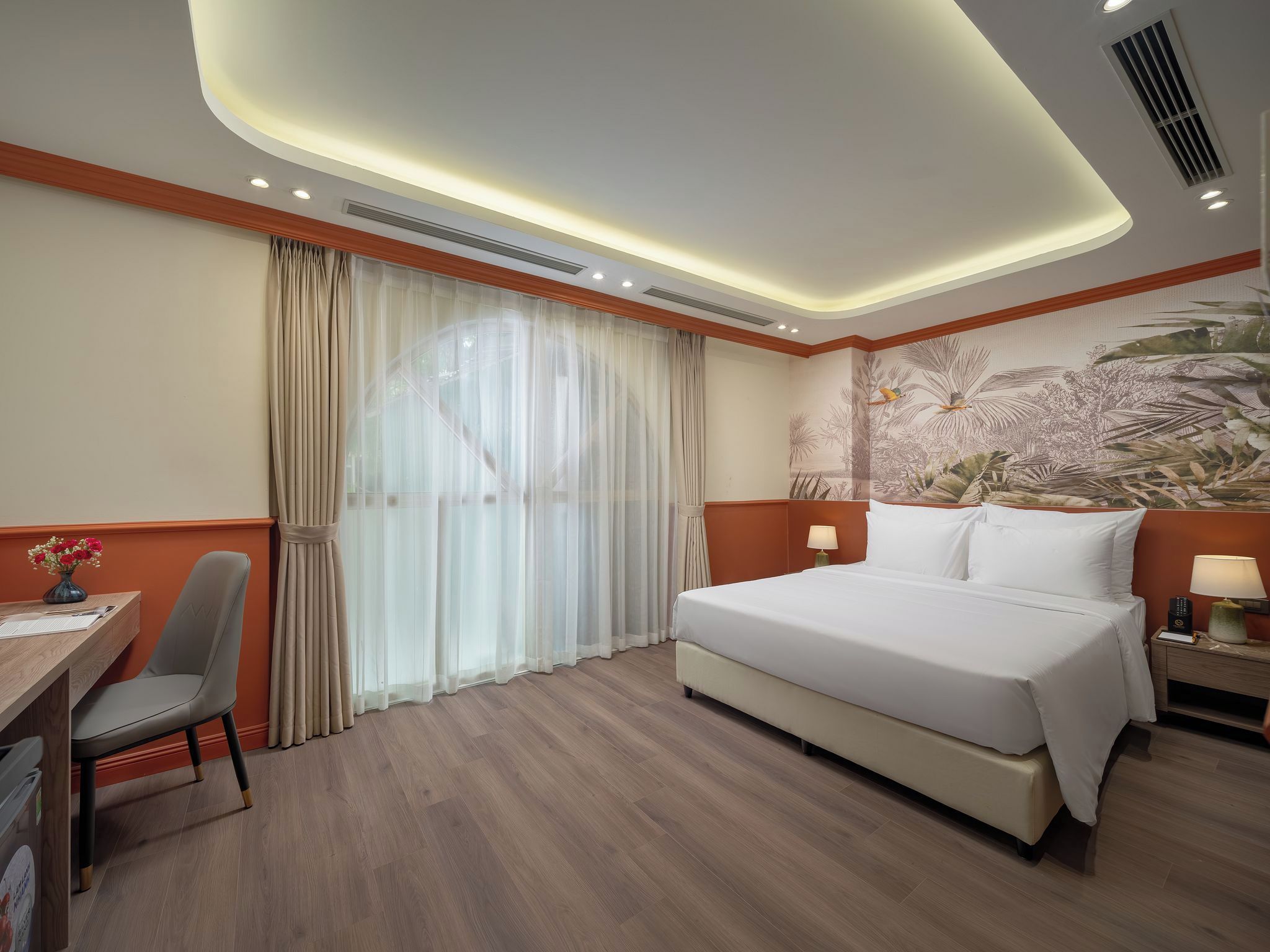 A hotel room with a bed, a desk, a chair, a nightstand, and a wall with a nature-themed mural.