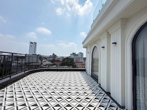 Un balcón con piso de baldosas geométricas, baranda de metal y vista a edificios distantes.