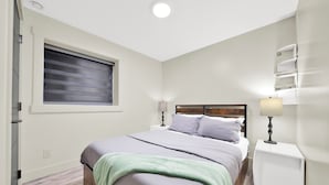 A bedroom with a bed, bedside tables, a window with blinds, and a ceiling light.