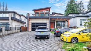 A modern two-story house with a garage, a paved driveway, and two parked cars.
