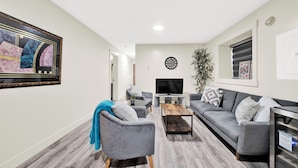 A living room with a grey sofa, a blue armchair, a coffee table, a TV, and a painting on the wall.