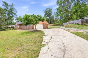 A residential driveway leading to a brick house with a garage, surrounded by a grassy lawn and trees.