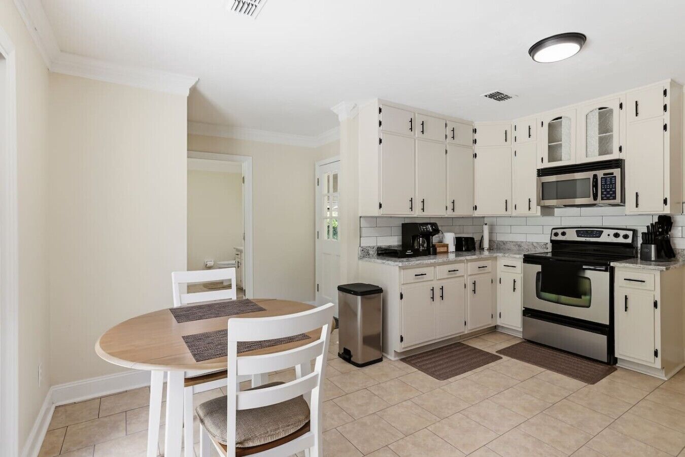 A compact kitchen with white cabinets, a microwave, an oven, and a dining area with a table and chairs.