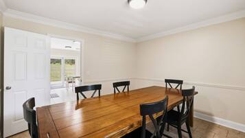 A dining room with a wooden table and six chairs, a white door, and a view of a lawn.