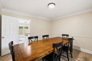 Een eetkamer met een houten tafel, zes stoelen, een witte deur en uitzicht op een gazon.