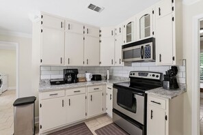 A modern kitchen with white cabinets, a built-in microwave, a stove, and a coffee maker.