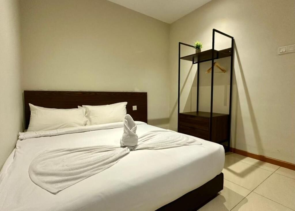 A neatly made bed with a white comforter and pillows, a wooden headboard, and a small plant on a black shelf beside the bed.