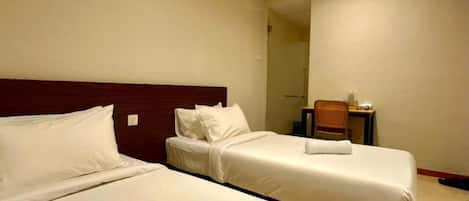 Une chambre d’hôtel avec deux lits, une tête de lit en bois, une petite table et une chaise.