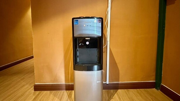 Un dispensador de agua en un pasillo con piso de madera y paredes anaranjadas.