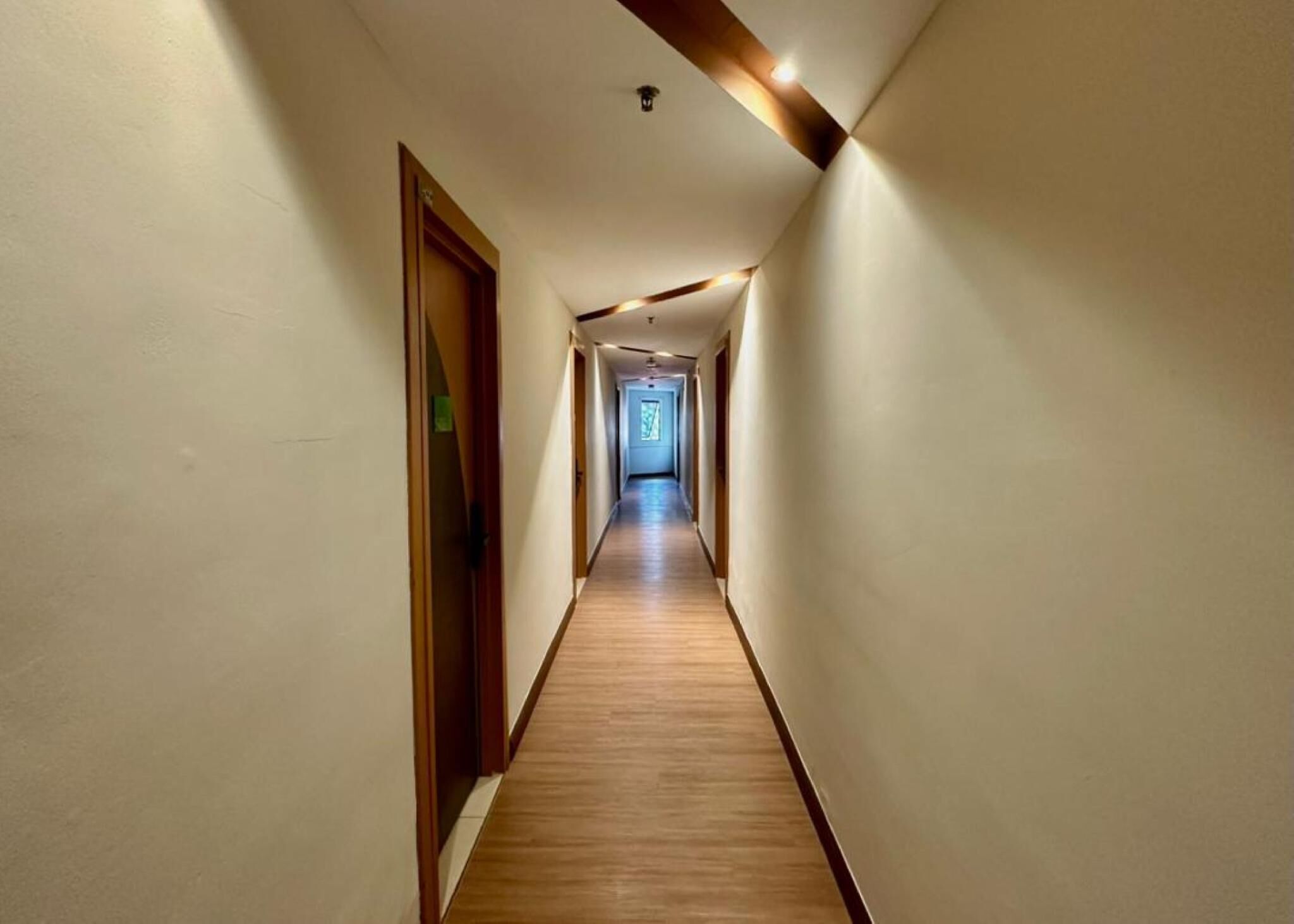 A long, narrow hallway with wooden flooring and white walls, leading to a door at the end.