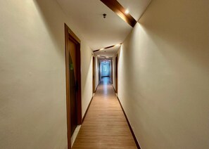 Un pasillo largo y estrecho con suelo de madera y paredes blancas, que conduce a una puerta al final.