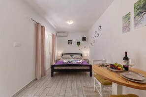 A bedroom with a bed, a bedside table with a wine bottle, and a dining area with a table set for two. - Zadar Studio Klaric 2 /w Garden, Zadar, Croatia (Zadar)
