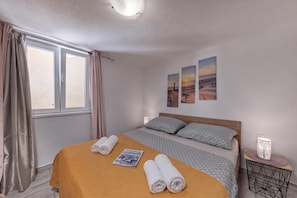 A hotel room with a bed, two pillows, a window with curtains, and wall art. - Zadar App Klaric 1 with Garden, Zadar, Croatia (Zadar)