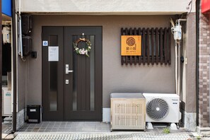 A hotel entrance with a dark brown door, a small sign, a wall-mounted air conditioning unit, and a wooden panel with a logo. - Midoribashi (Osaka)
